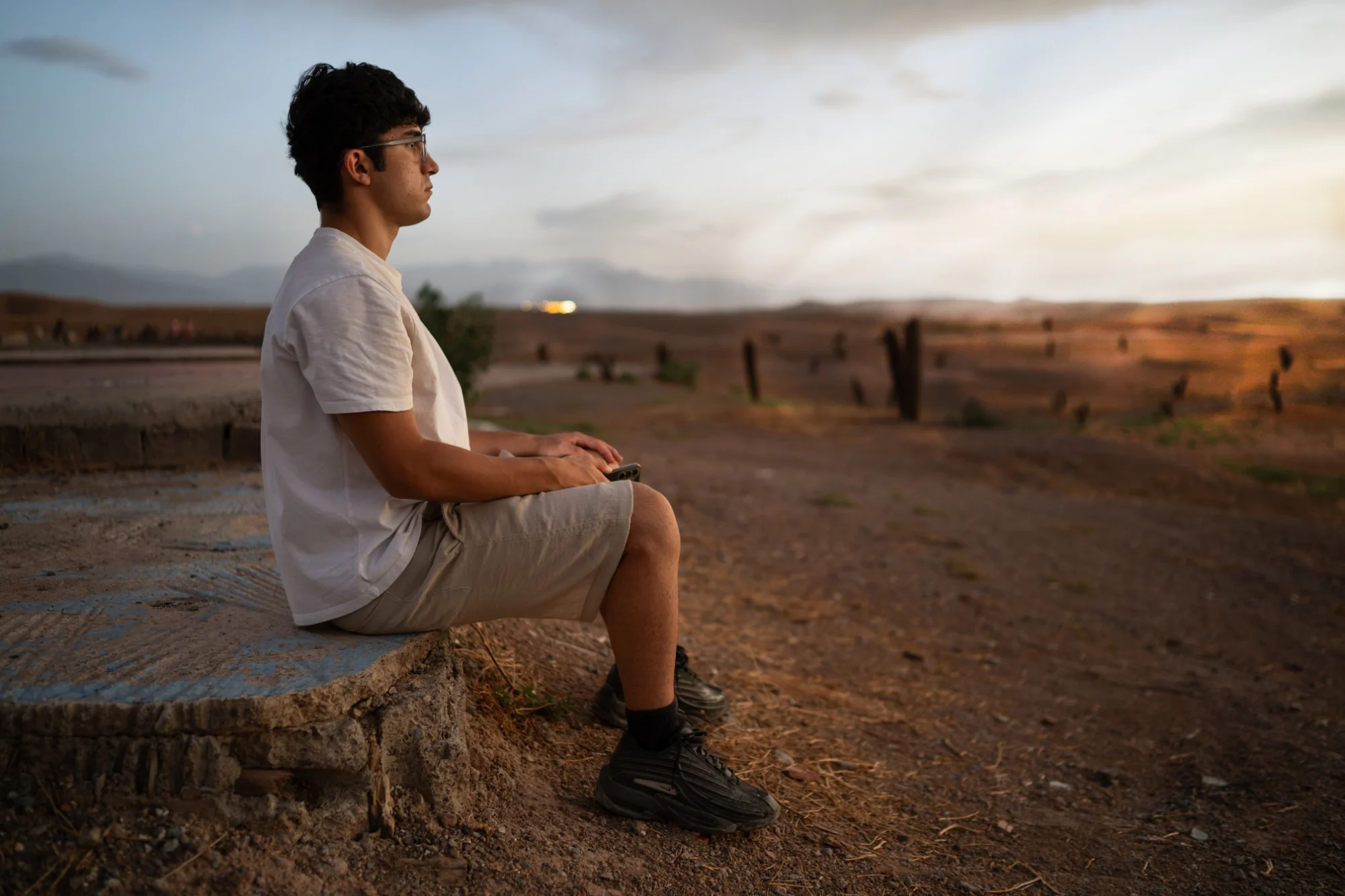 A young person sitting alone and looking over an open landscape at sunset, photographed by Massimo Parisi.