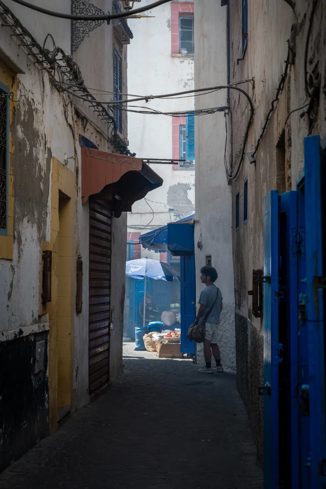 A person standing in a narrow alley between weathered walls and blue doors.